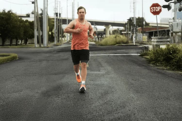 Atleta com síndrome de Down corre em uma rua calçando o tênis laranja da Adidas
