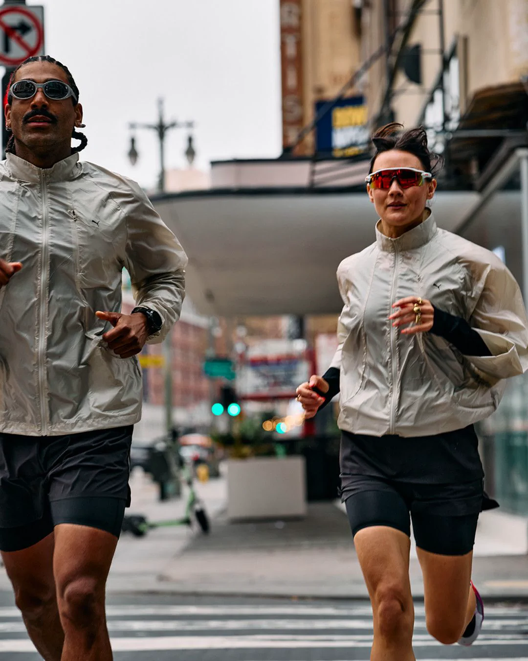 Dois corredores atravessam uma avenida durante um treino de corrida de rua na cidade