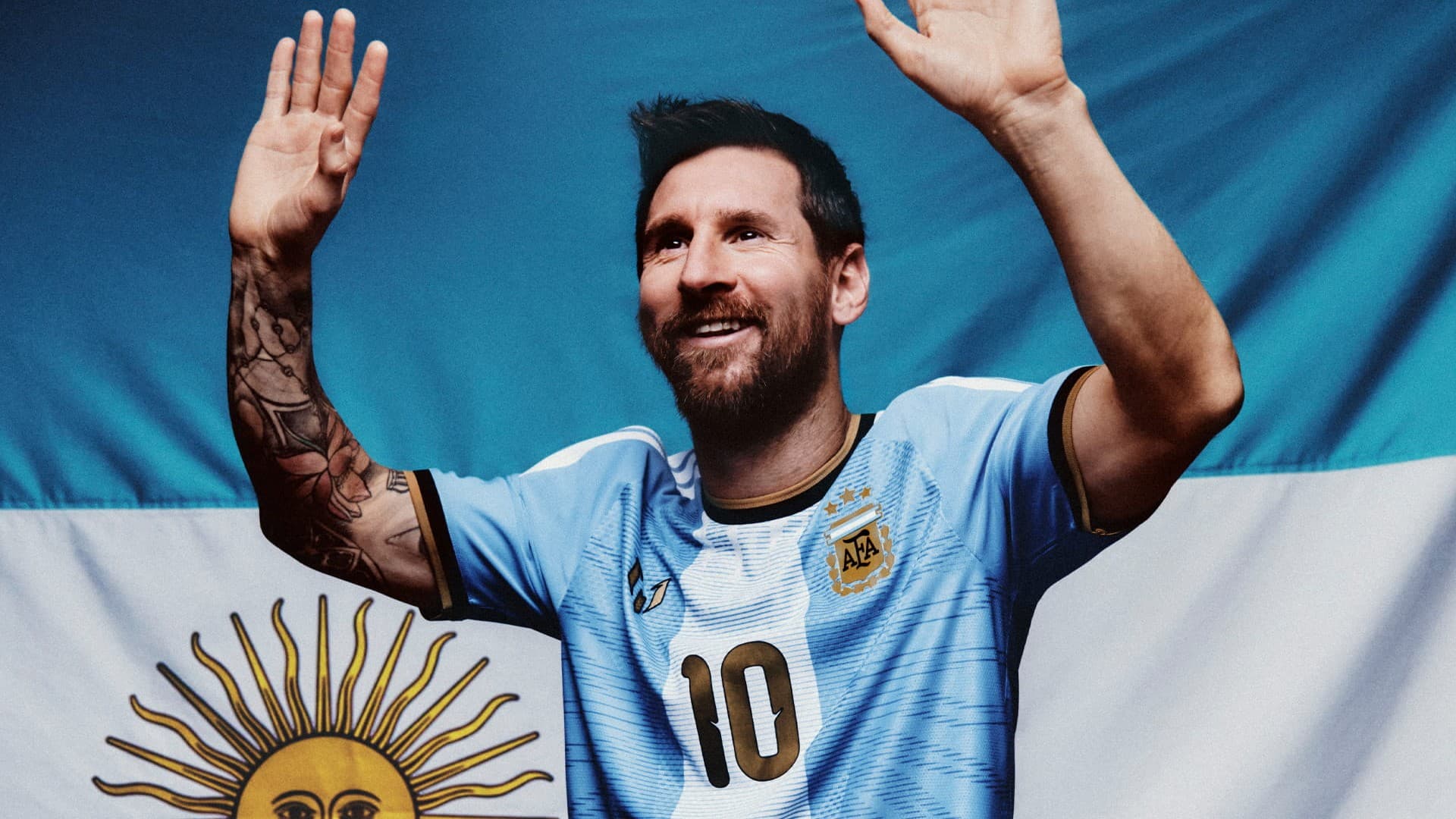 Lionel Messi acena com as duas mãos vestindo a camisa especial de despedida da Argentina, diante de uma bandeira argentina com o Sol de Maio