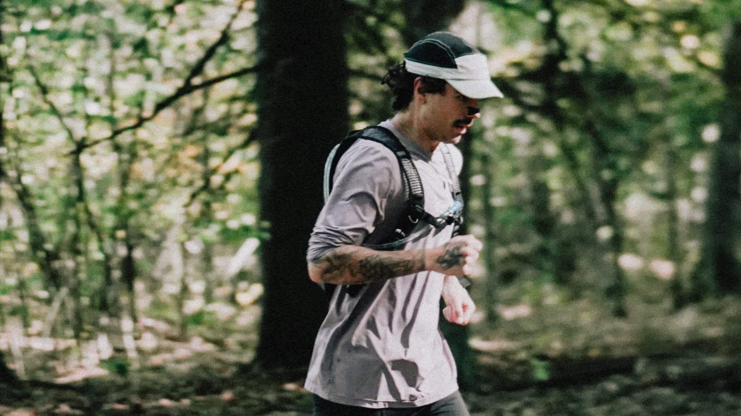 Pedro Nogueira corre por uma trilha de floresta em Pineland Farms, de viseira e mochila de hidratação