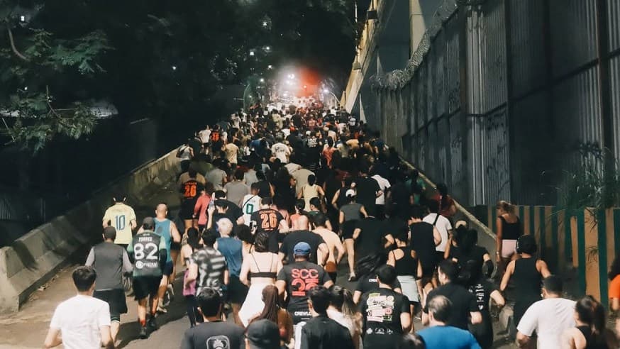 Centenas de corredores sobem uma rampa iluminada à noite em Belo Horizonte, num treino do Calma Clima