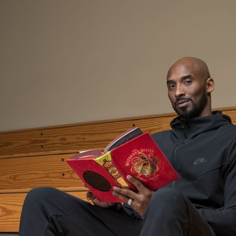 Kobe Bryant sentado numa arquibancada de madeira, lendo um livro.