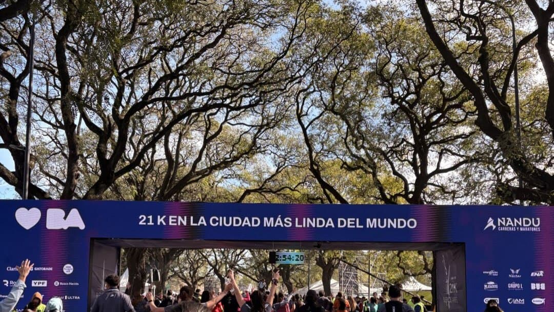 Arco de chegada azul da Meia Maratona de Buenos Aires com a frase 21K en la ciudad más linda del mundo, sob árvores