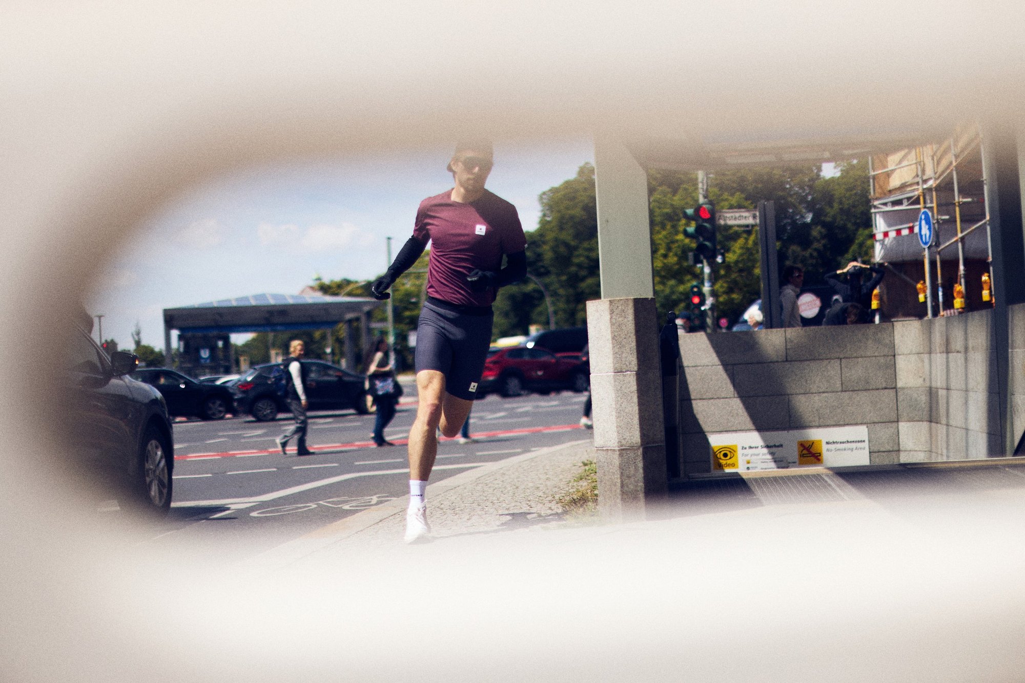 Corredor de camiseta bordô e shorts escuros atravessa uma rua de Copenhague, fotografado através de uma abertura arredondada