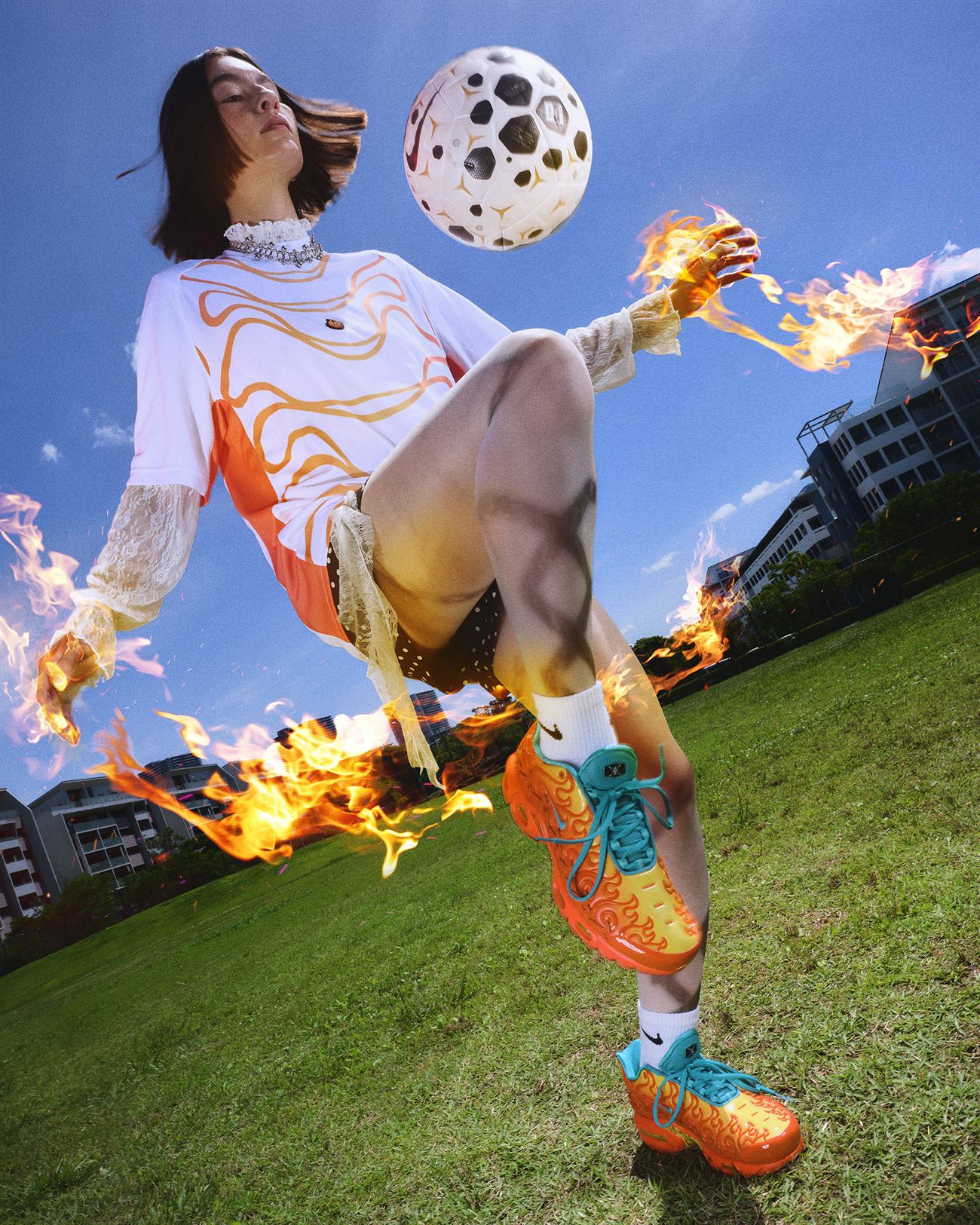 Mulher domina uma bola de futebol com chamas saindo das mãos e das pernas, calçando o Air Max Plus laranja da coleção Mera Mera no Mi