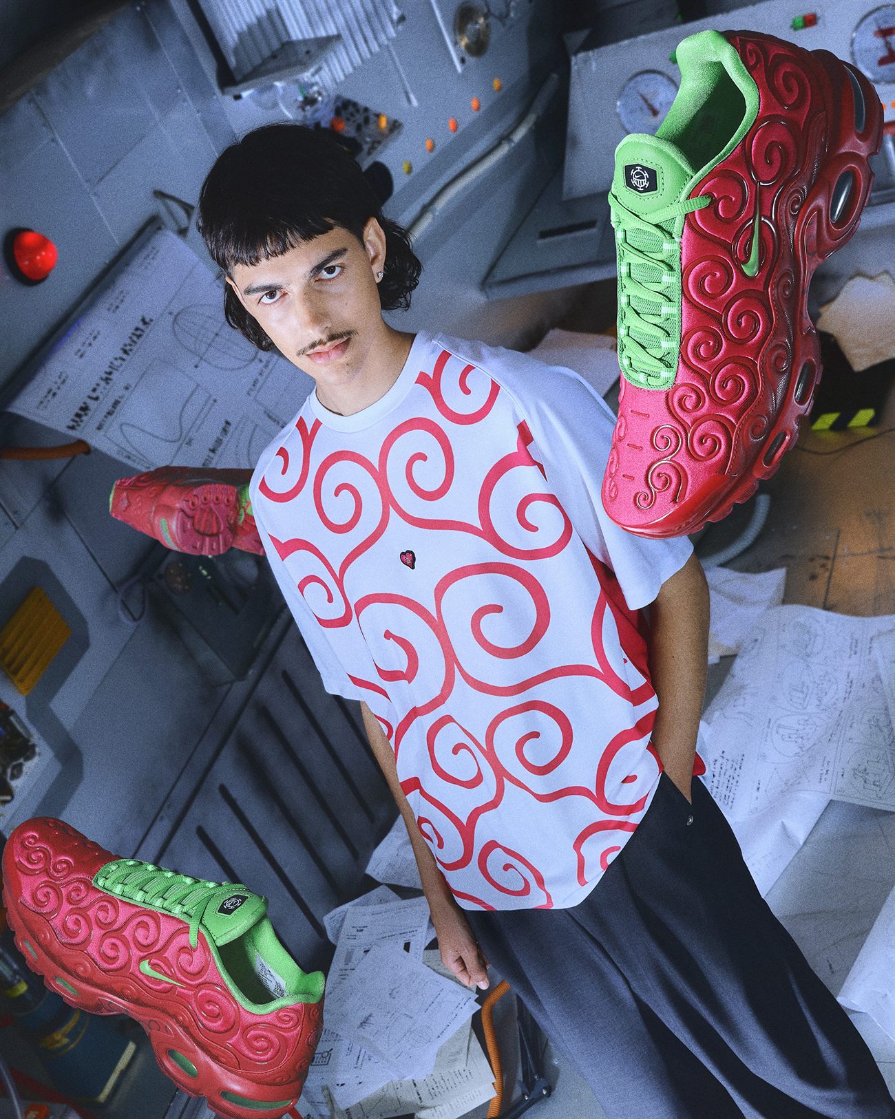 Rapaz de camiseta branca com espirais vermelhas cercado por três pares do Air Max Plus vermelho e verde da versão Ope Ope no Mi