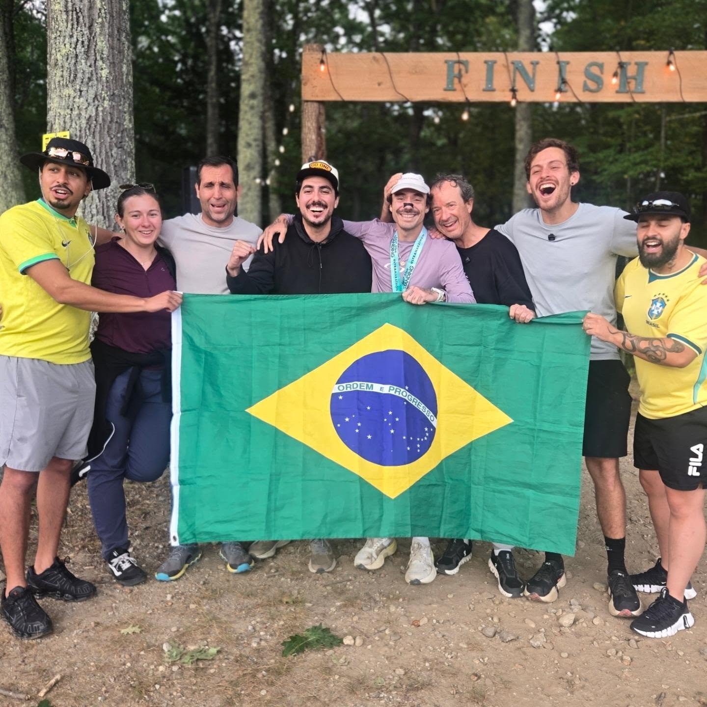 Pedro Nogueira e a equipe brasileira seguram a bandeira do Brasil embaixo do arco de chegada do Last Man Standing
