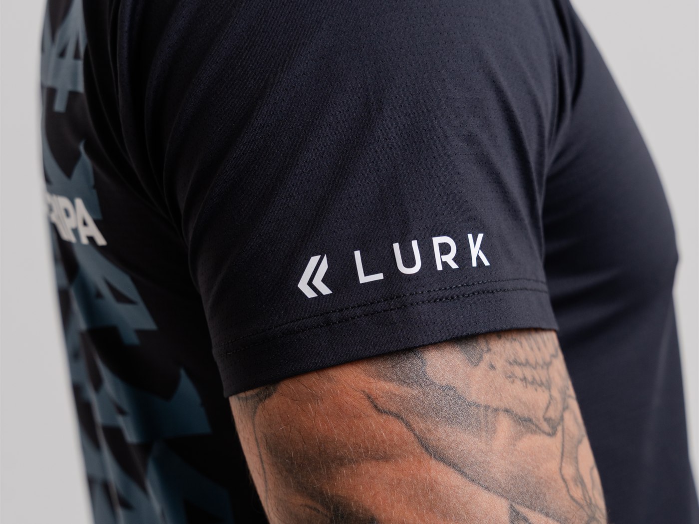 Manga da camiseta preta com a assinatura Lurk aplicada em branco