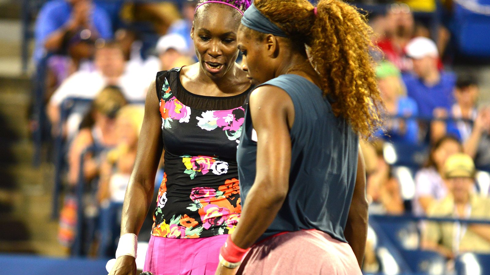 Venus e Serena Williams lado a lado durante partida de duplas no US Open de 2013, Venus de regata florida e Serena de regata cinza