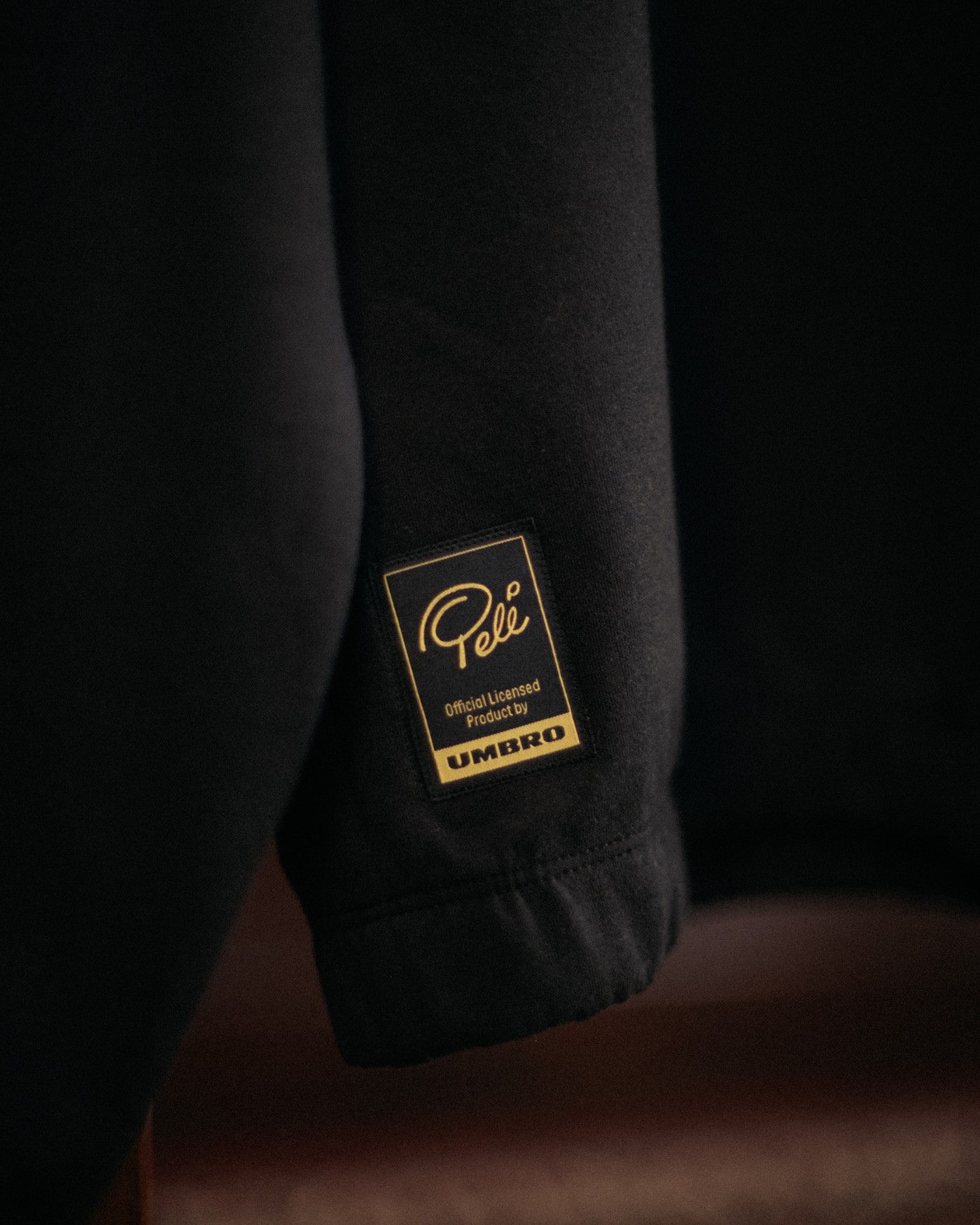 Detalhe da manga de uma peça preta com etiqueta dourada que traz a assinatura de Pelé e o logo da Umbro